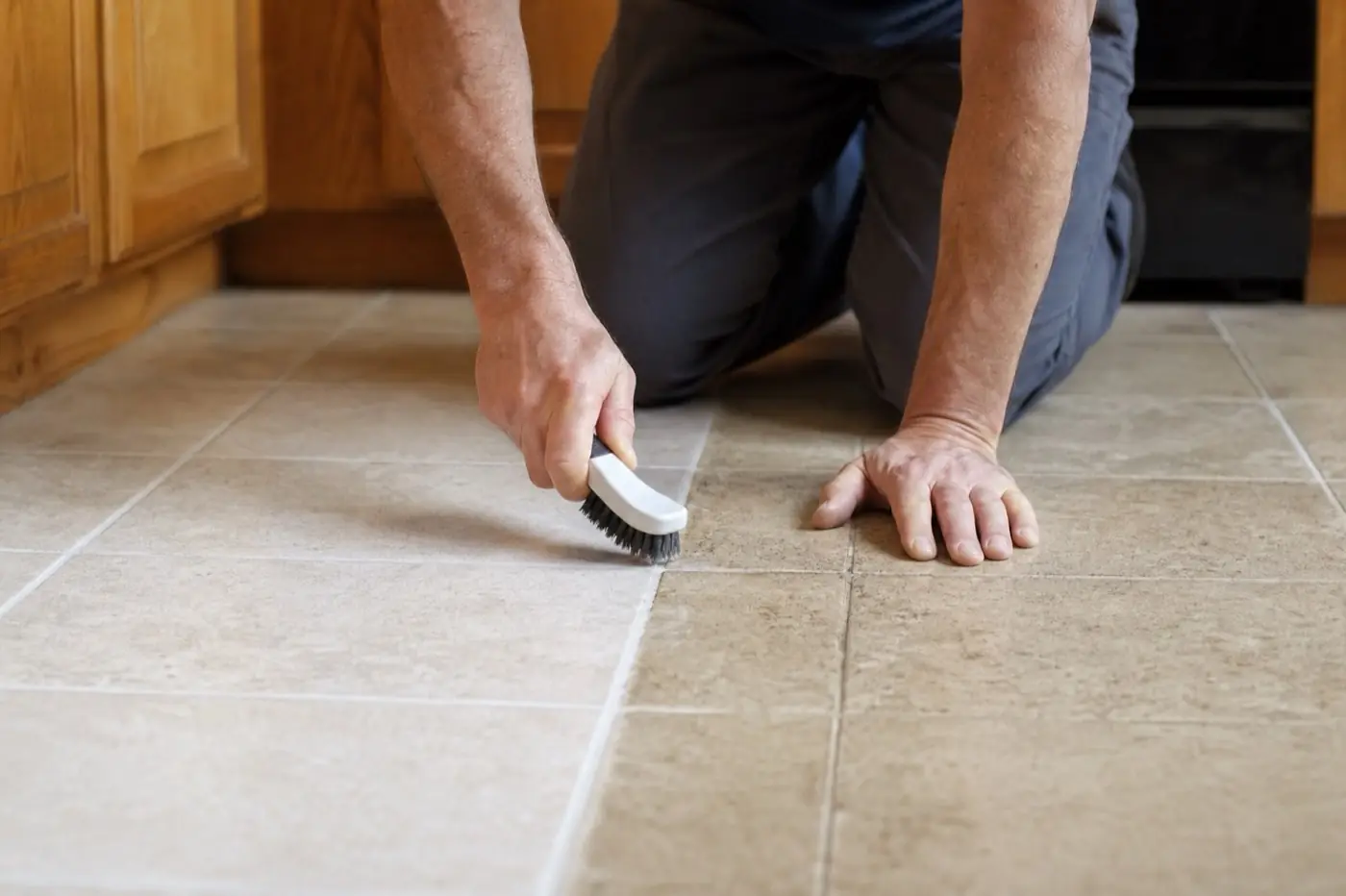 AI-generated image: a person on their knees scrubbing kitchen tile grout lines with a brush.