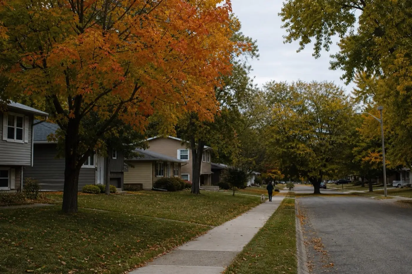 AI-generated image: a quiet residential street with maple trees turning orange and modest split-level homes.